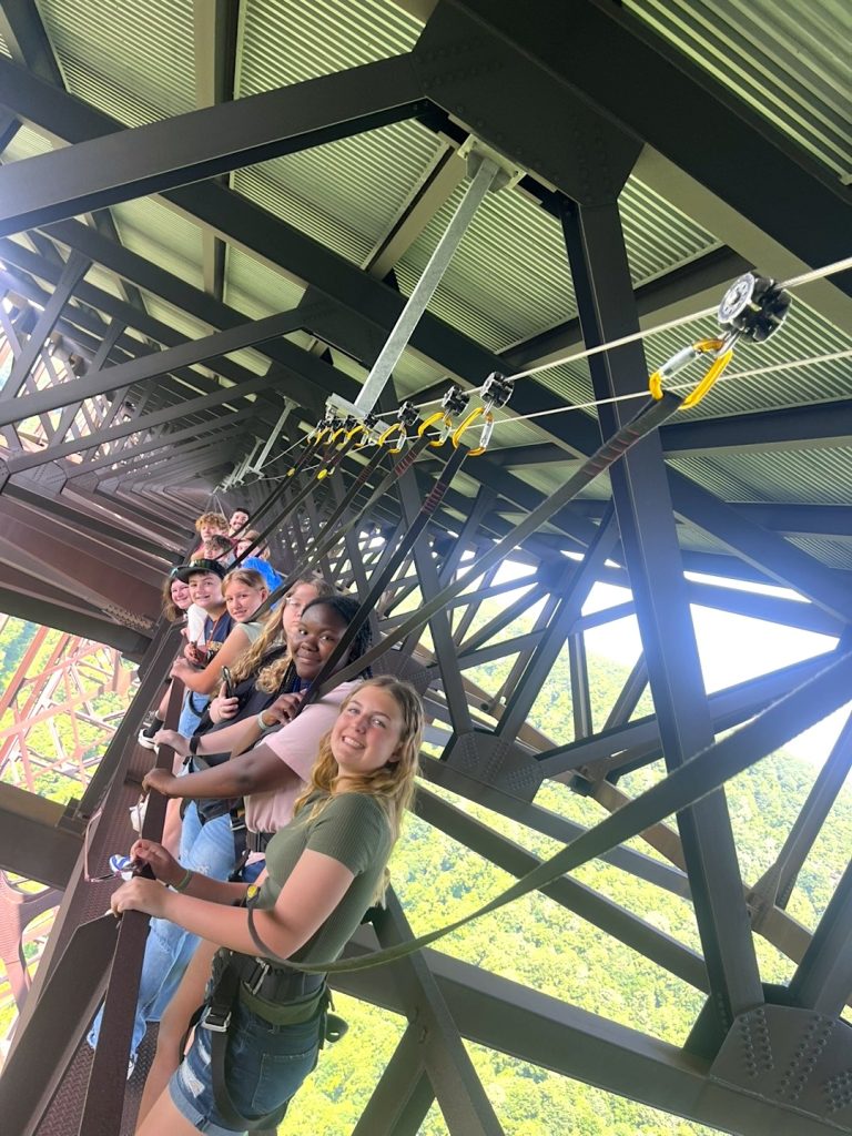 Smiling students harnessed under large steel arch bridge the New River Gorge Bridge