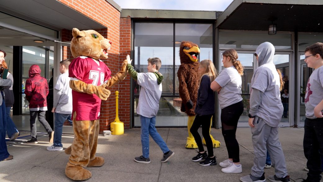 Mascot Mt Lion and mascot hawk giving high fives to students walking