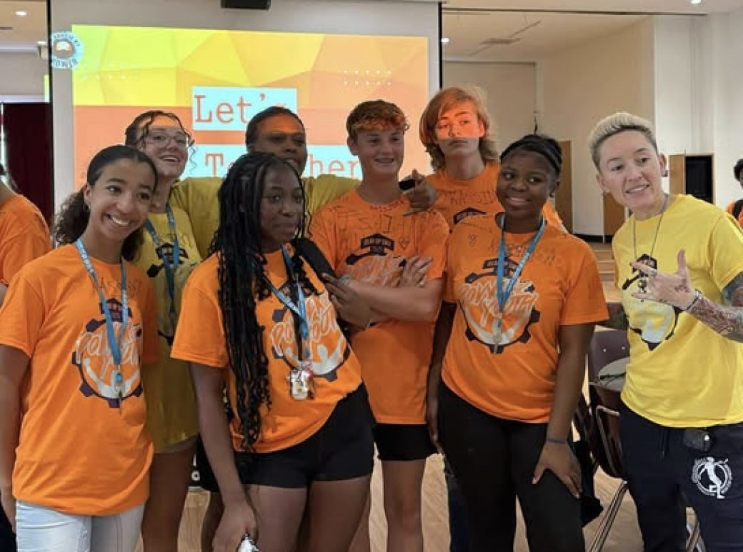 Students in orange shirts smiling beside counselors in yellow shirts