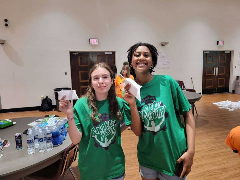 Two girls standing holding paper while smiling