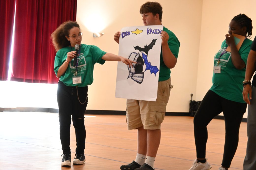 group of campers in green present their poster to the rest of the campers